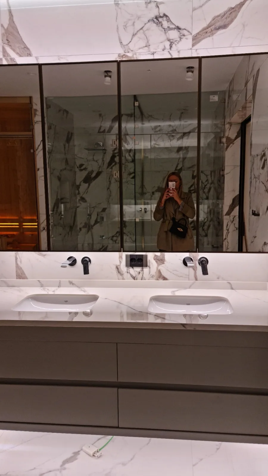 Calacatta mermer kaplı banyo; çift lavabolu vizon rengi asma dolap, tam boy aynalı üst dolaplar ve cam kabinli duş