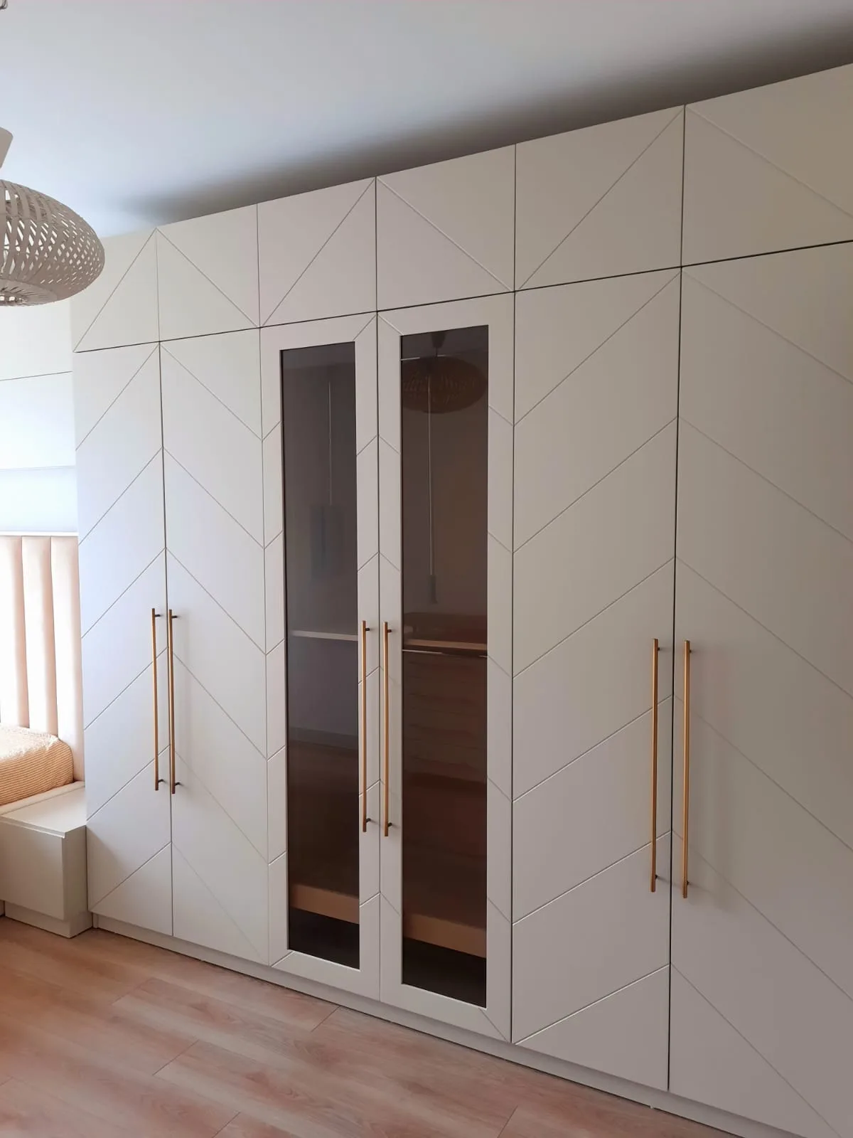 Krem renkli, çapraz desenli kapaklı ölçüye özel gardırop; ortada camlı modül