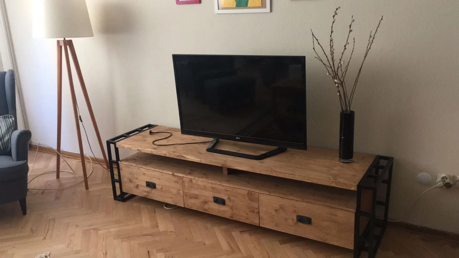 Ahşap gövdeli, siyah metal ayaklı çekmeceli TV sehpası; balık sırtı parke zemin