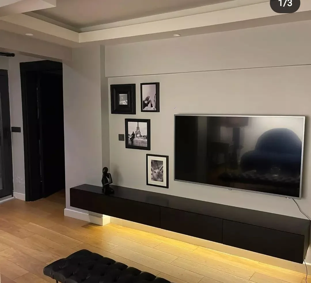 Duvara asılı siyah TV ünitesi; alt LED aydınlatma ve tablo duvarı