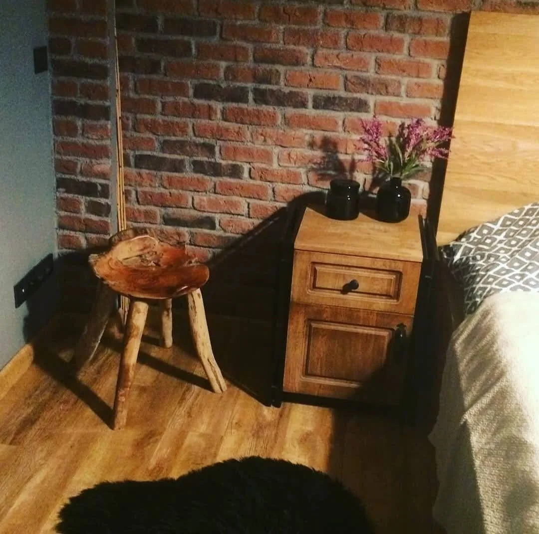 Tuğla duvar önünde ahşap komodin ve kütük sehpa ile rustik yatak odası düzeni