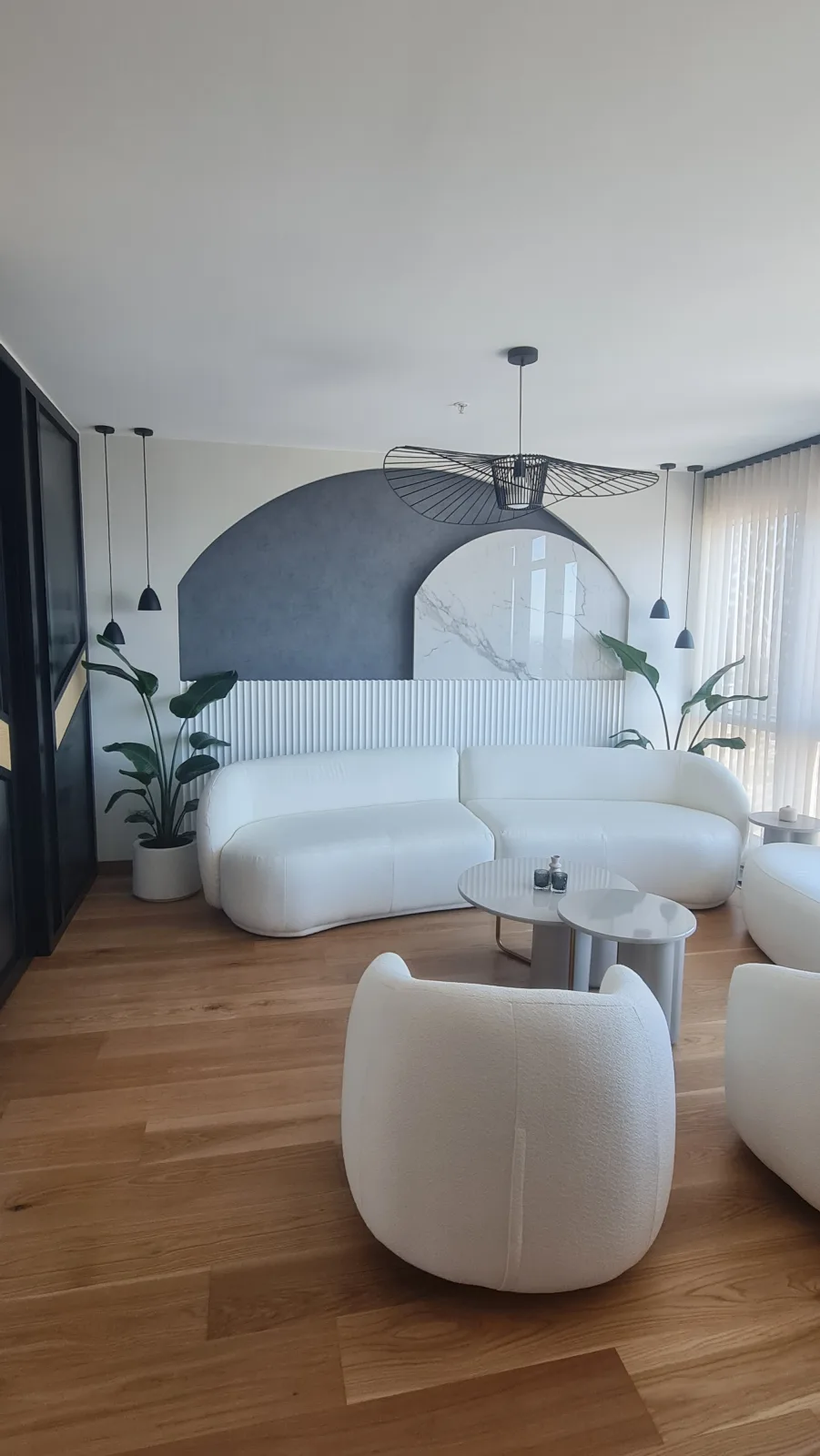 Beyaz bukle kumaşlı kavisli kanepe ve yuvarlak formlu tekli koltuklar; kemerli niş duvarı ve mermer panel